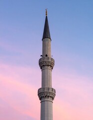 Tall Minaret with Gray Bricks and Gold Spire Against Colorful Sky at Sunset