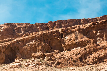 Fototapeta premium Layered rock formations and arid mountain slopes in Hormozgan, Iran, revealing striking geological textures beneath a clear blue sky. 