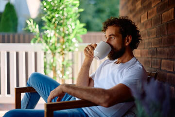 Mid adult man drinking coffee while relaxing on porch.
