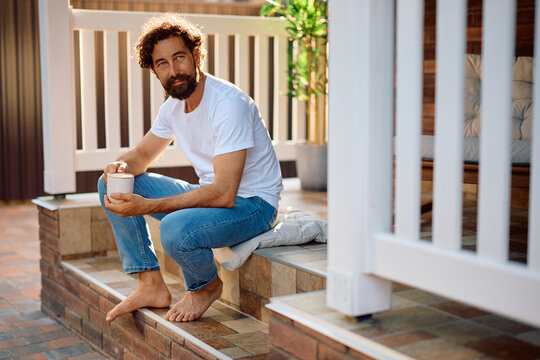 Mid adult man having cup of coffee while sitting on staircase in front of his house.