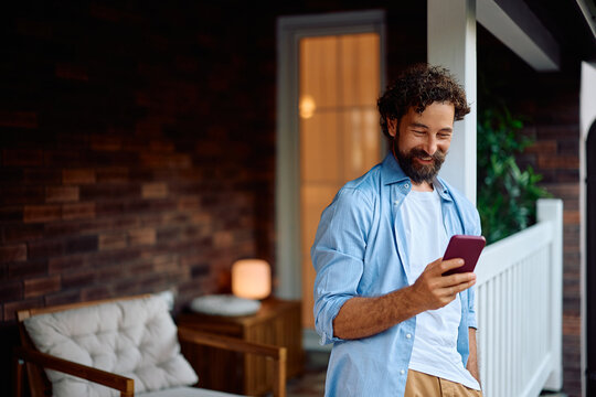 Happy man using cell phone on front porch.