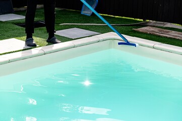 Person cleaning a residential swimming pool with a skimmer during a sunny afternoon