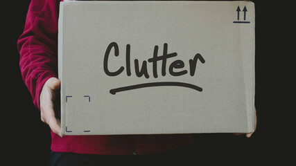 A person holding a cardboard box with clutter written on the front. Decluttering, moving, cleaning, and organization background. Streamline or simplify design element.