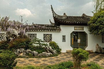Traditional Chinese garden pavilion with ornate roof, lattice windows, flowering wisteria, and rock landscaping at Kunming Horti Expo Garden in Yunnan, China