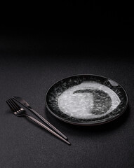 Empty round black plate for food, kitchen utensils on dining table. Empty plate