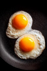 Two sunny side up eggs sizzle in a black skillet on the stovetop, showcasing bright yellow yolks and slightly crispy edges, perfect for breakfast