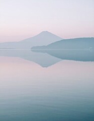 Obraz premium Tranquil Lake Reflecting Mountain Silhouettes in Soft Hues of Blue and Pink