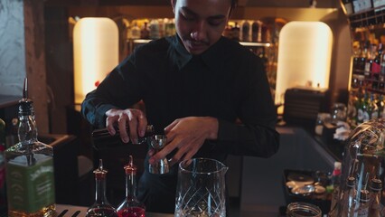Portrait good looking Asian bartender using jigger measure liquor syrup into mixing glass preparation at luxurious beverage counter bar, neat professional barman costume at nightclub luxury. Vinosity.