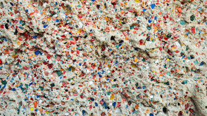 Close-up view of a concrete wall showcasing colorful glass fragments embedded within the surface, forming a vibrant mosaic-like texture that adds visual interest and artistic flair.