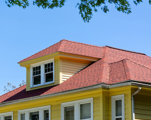 Vibrant yellow house with red roof and dormer window on a sunny day in Brighton, Massachusetts, USA

