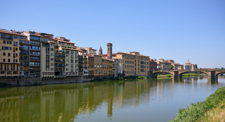 Scenic view of the Arno River and Ponte Santa Trinita bridge with colorful riverside buildings in Florence, Italy, under clear summer sky 