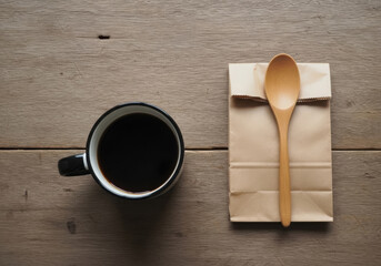 Overhead view of coffee cup and paper bag with spoon on wooden table