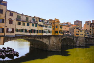Panoramic view of Ponte Vecchio bridge with colorful buildings and small boats floating below on the Arno River in Florence, Italy, on a sunny summer day 
