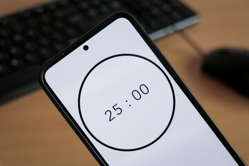 A phone with white 25-minute timer to study with pomodoro method on laptop keyboard, study business background