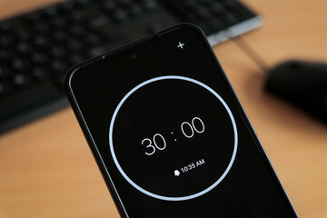 A phone with a black and white 30-minute timer to study and be productive on laptop keyboard, study business background