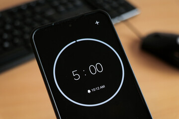 A phone with a black and white 5-minute timer to study and be productive on laptop keyboard, study business background
