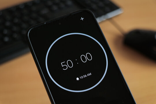 A phone with a black 50-minute timer to study with pomodoro method on laptop keyboard, study business background - Powered by Adobe