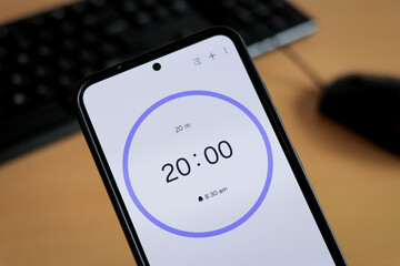 A phone with a black and white 20-minute timer to study with pomodoro method on laptop keyboard, study business background