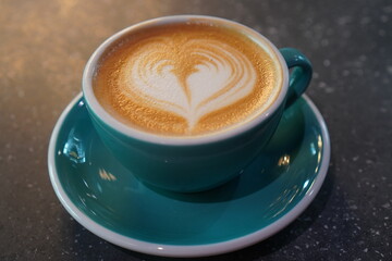 Delicious cappuccino with heart latte art served in a turquoise cup at a cozy cafe