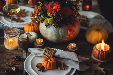 Elegant atmospheric beautiful dinner table setting for thanksgiving or wedding celebration, fall countryside style, pumpkins as decor. Romantic cozy home atmosphere. Wine, floral pumpkin centrepiece.