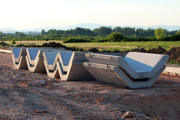 V-shaped precast concrete sections are neatly stacked at a construction site, ready for assembly in a major drainage or irrigation infrastructure project on cleared earth