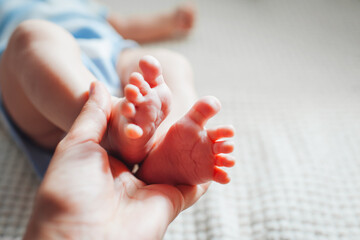 Mother holds newborn baby's feet in hand. Infant sleeping on bed. Close up of little toes
