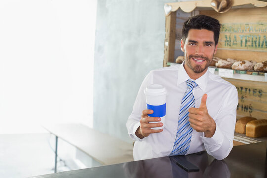 Male office worker sitting at bakery cafe counter holding coffee cup with sleeve giving thumbs-up