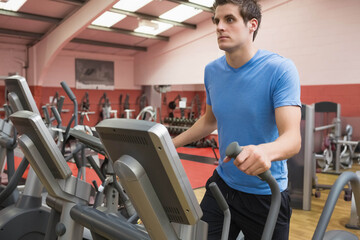 Man exercising on elliptical trainer at commercial gym with dumbbell rack and benches, copy space