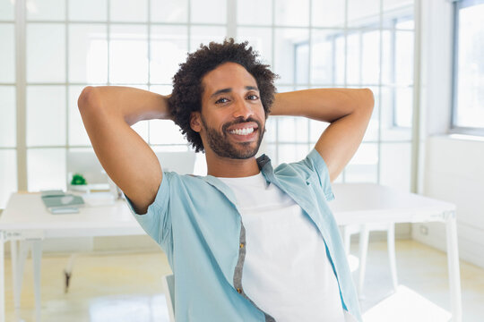 Mid adult African American man leaning back in chair at modern office desk with green notebook - Powered by Adobe