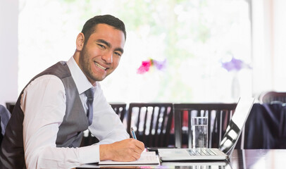 Man in business attire taking notes at cafe table with laptop and notebook, copy space