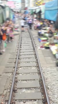 SAMUT SONGKHRAM, THAILAND - AUGUST 2024 : View of Maeklong railway market. Tracking shot from train drivers seat. Famous market for tourists. Time lapse shot.