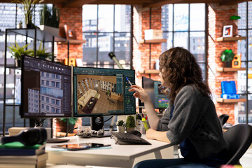 Female arranging virtual assets in a architectural software on dual monitors, creating a detailed 3D render of a floor plan. Woman uses the program for computer aided interior design.