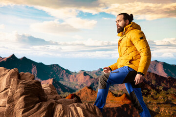 Hiker gazes at the panoramic view of dramatic mountain peaks and clouds, feeling the thrill of adventure and rewards of perseverance. The journey represents strength and personal growth.