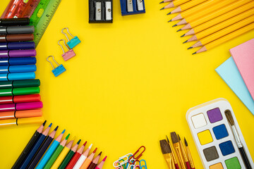 Flat lay of colorful school and art supplies on yellow background with copy space.