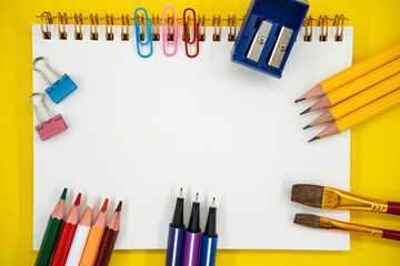 Flat lay of school and art supplies with blank notebook on yellow background with copy space.