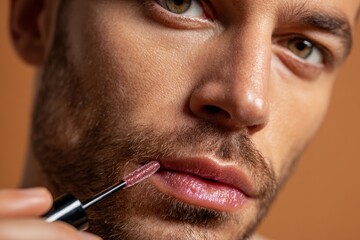 Man poised to enhance his lips with a glossy sheen, showcasing beauty and confidence against a warm beige background