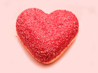 A heart-shaped doughnut with sprinkles on top sits on a pink card. The doughnut is the main focus of the image, and the pink card adds a touch of romance and sweetness to the scene