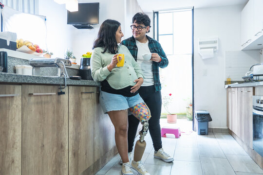 Pregnant woman with prosthetic leg enjoying coffee with husband in kitchen