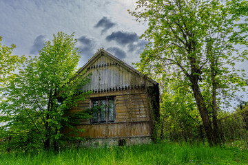 Old wooden house with green trees under a bright cloudy sky