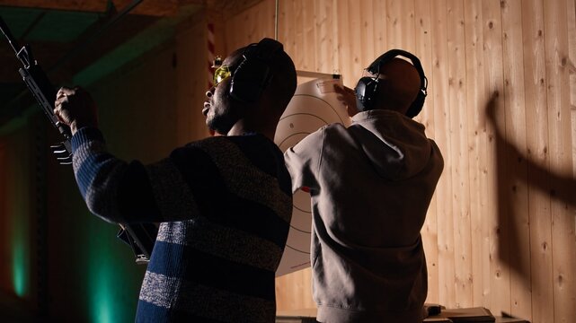 Man holds rifle, enjoying recreational shooting experience in firing range next to group of friends. People practicing with weapons in safe environment at shooting range company, camera A
