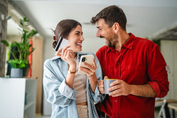 Happy couple making online shopping using smart phone and credit card at home