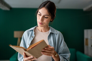 Young adult caucasian woman smiling and reading a book at home