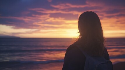 A person admires a colorful sunset at the beach, reflecting calmness and beauty in the evening sky over the ocean waves.