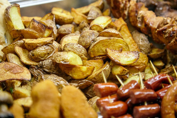 Golden-brown roasted potato wedges arranged neatly on a serving tray, accompanied by skewered sausages and crispy snacks, showcasing delicious comfort food options for gatherings