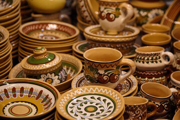 Colorful ceramic dishware collection featuring intricately designed plates, bowls, and cups stacked together, showcasing traditional craftsmanship and vibrant patterns in a warm setting