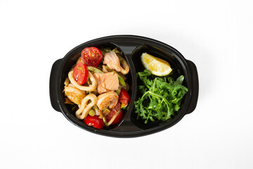 Seafood salad with arugula, cherry tomatoes, lemon, and pieces of fish and squid, served on a plate