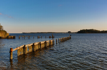 Fototapeta premium Broken wooden pier extending into calm coastal water at sunset