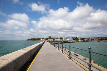 Looking along the pier of the harbour arm in Folkestone towards the beach and the town on a summer day.