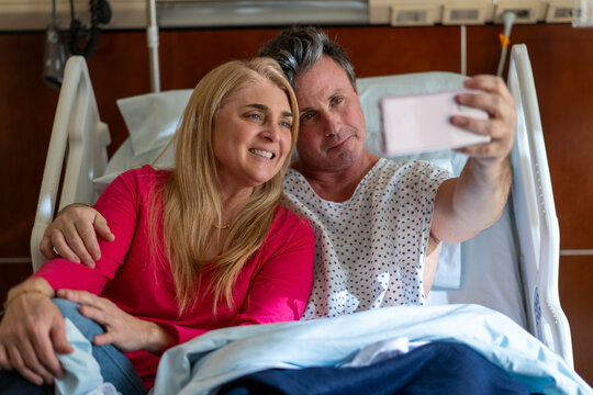 Smiling couple taking selfie in hospital bed
