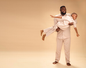 With arms outstretched and laughter in the air, an African father lifts his son mid-flight. Their matching cream outfits and glowing smiles capture a playful, love-filled moment of trust and joy.